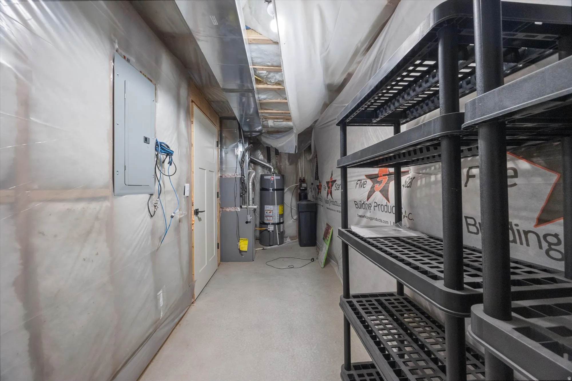 Unfinished below grade area featuring electric panel, a water softener system, heating unit, and strapped water heater