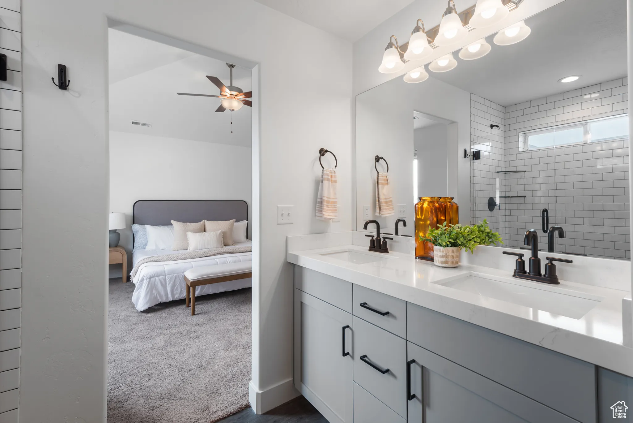 Ensuite bathroom featuring double vanity, tiled shower, and ceiling fan