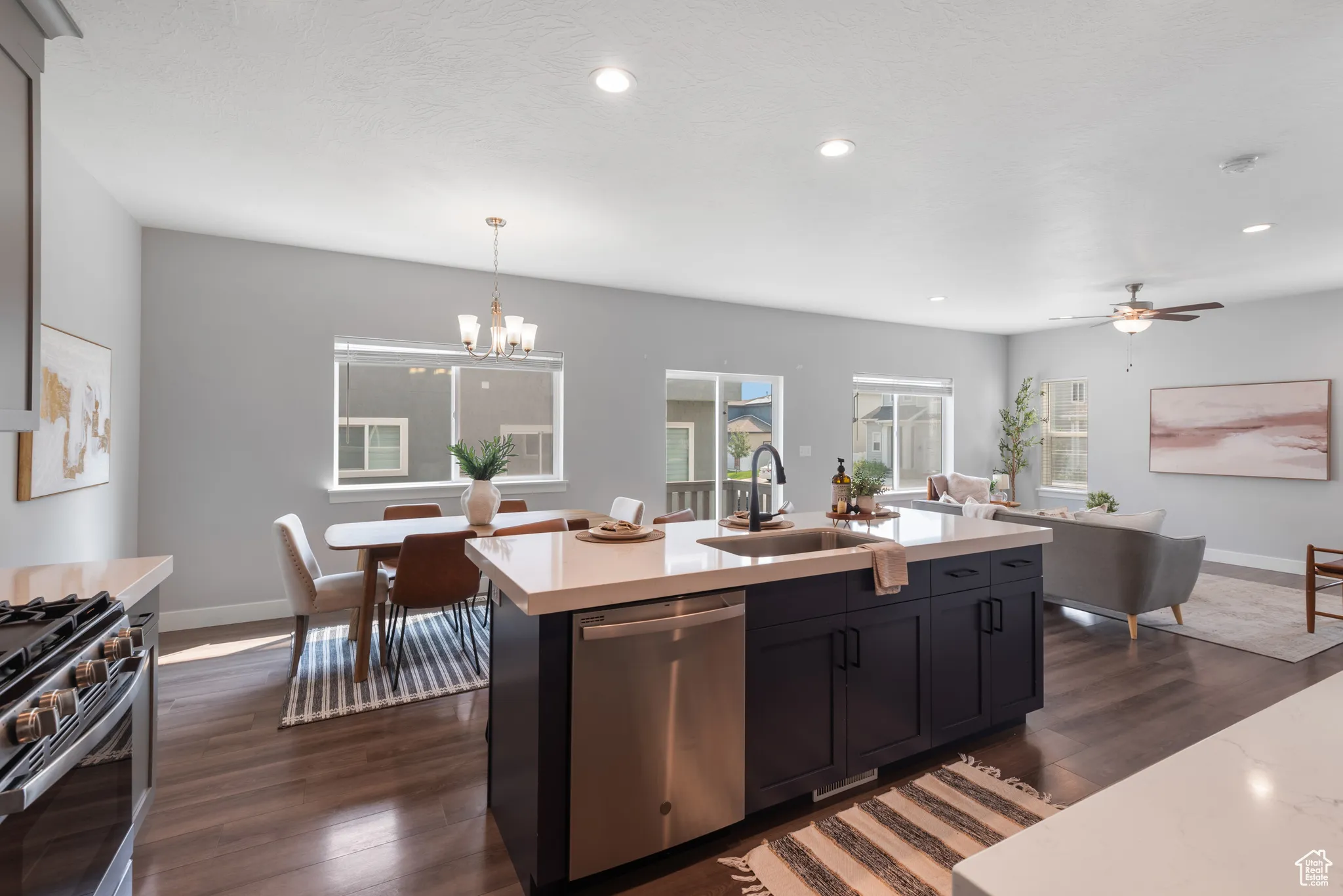 Kitchen with dishwasher, dark wood finished floors, hanging light fixtures, light stone countertops, and open floor plan