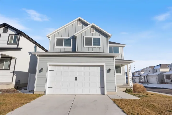 View of front of house with board and batten siding, an attached garage, concrete driveway, covered porch, and a front lawn