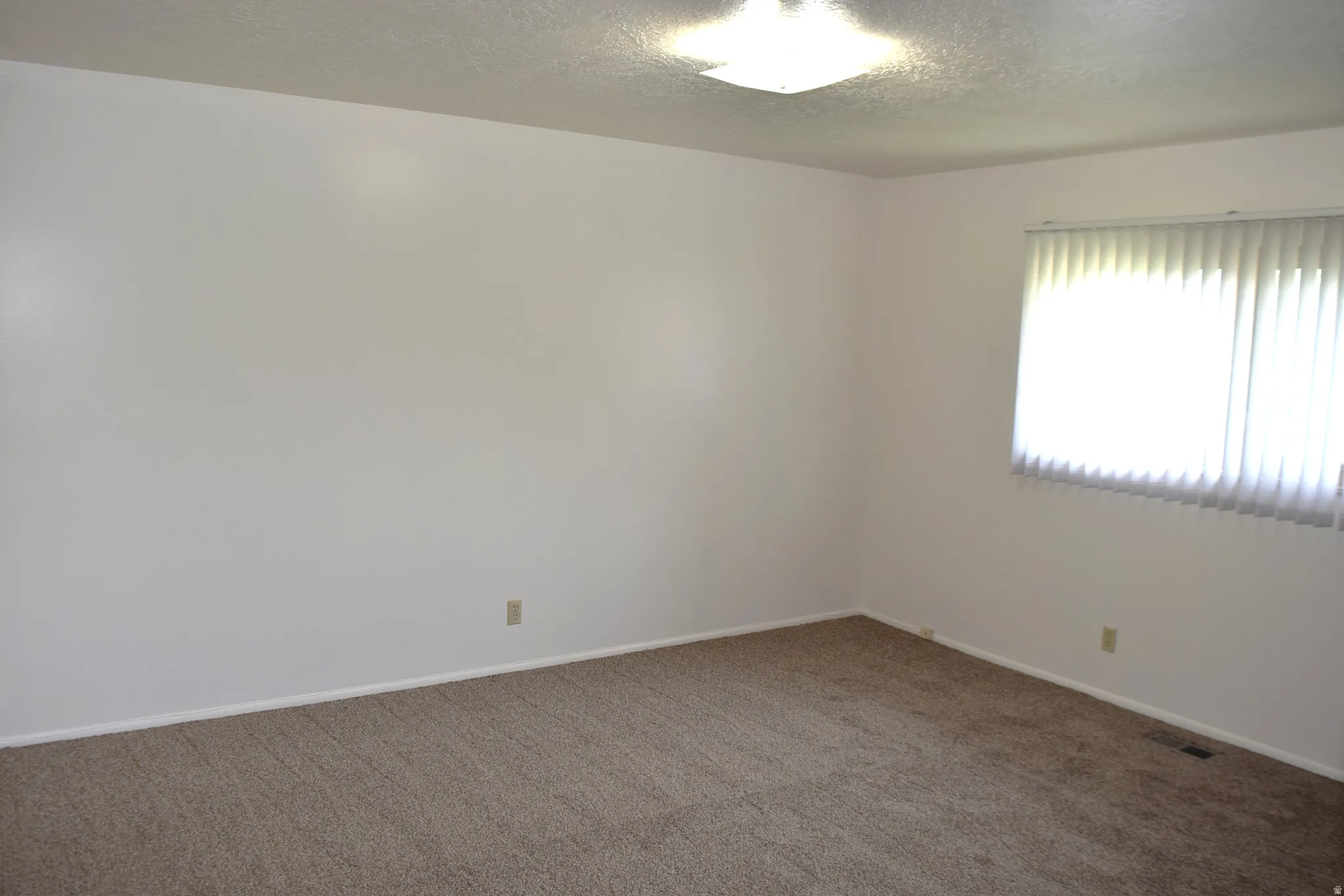 Carpeted empty room featuring a textured ceiling and baseboards