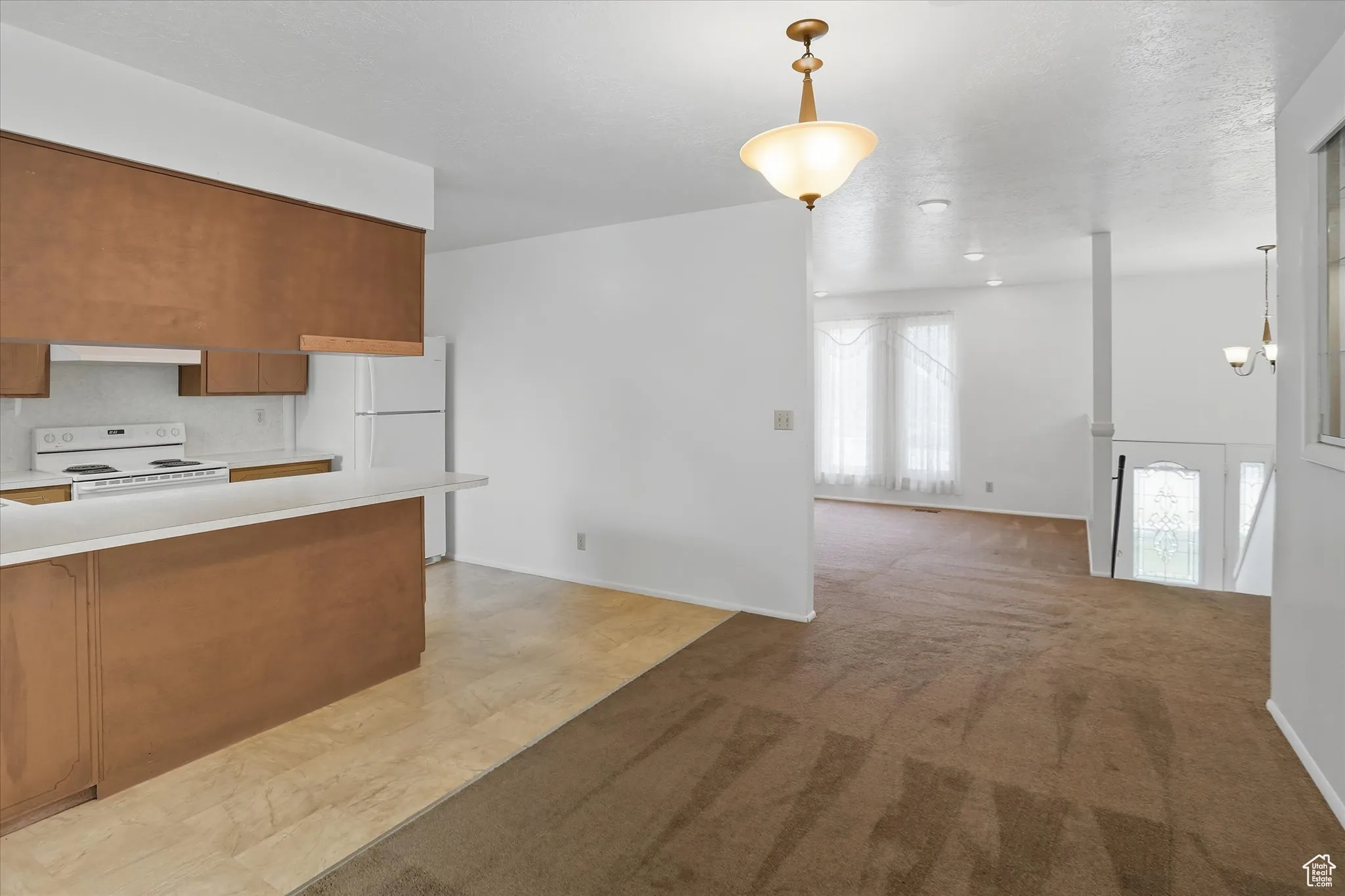 Kitchen with brown cabinets, light countertops, decorative light fixtures, and white appliances