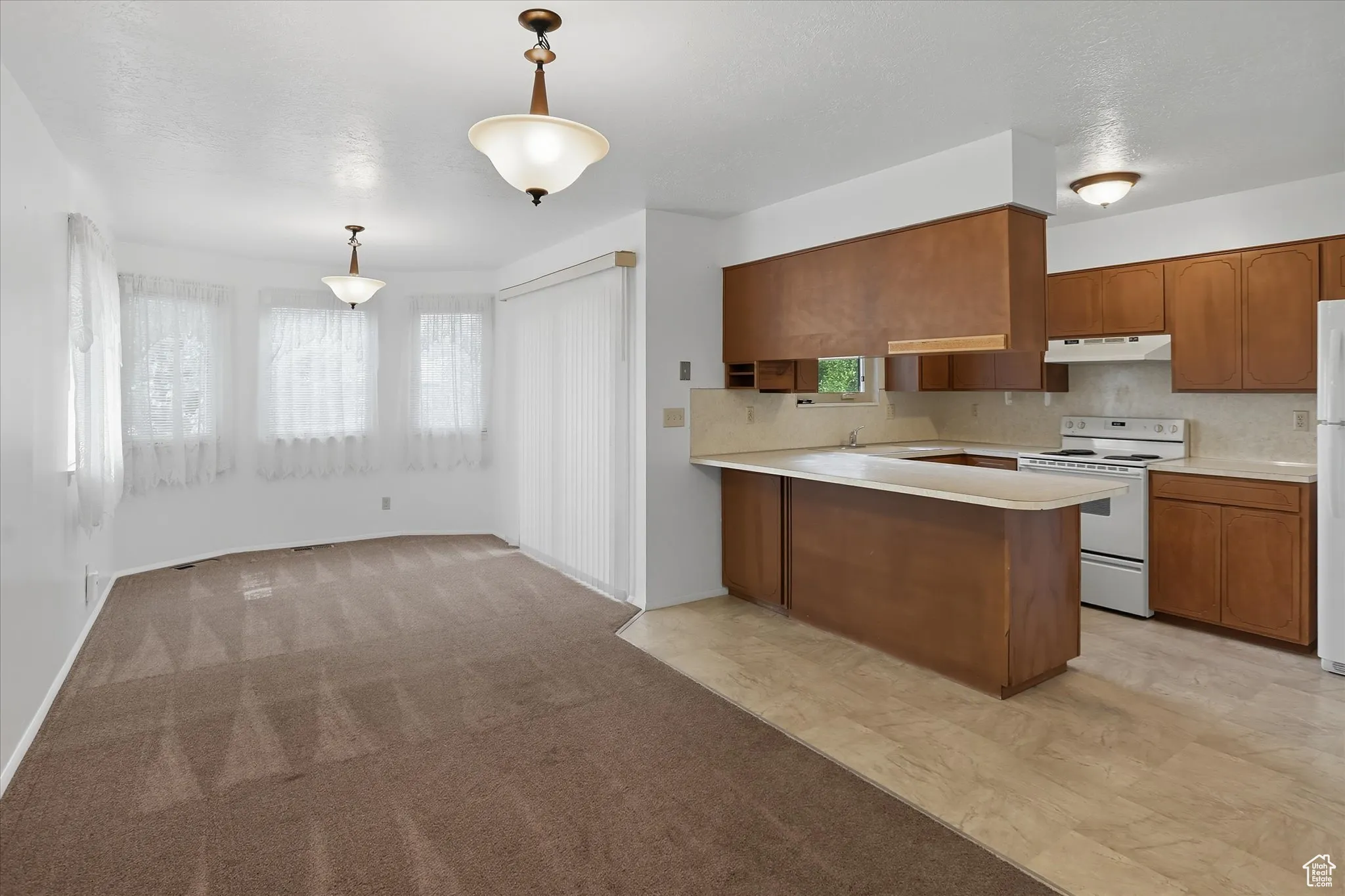 Kitchen featuring light countertops, white appliances, brown cabinetry, a peninsula