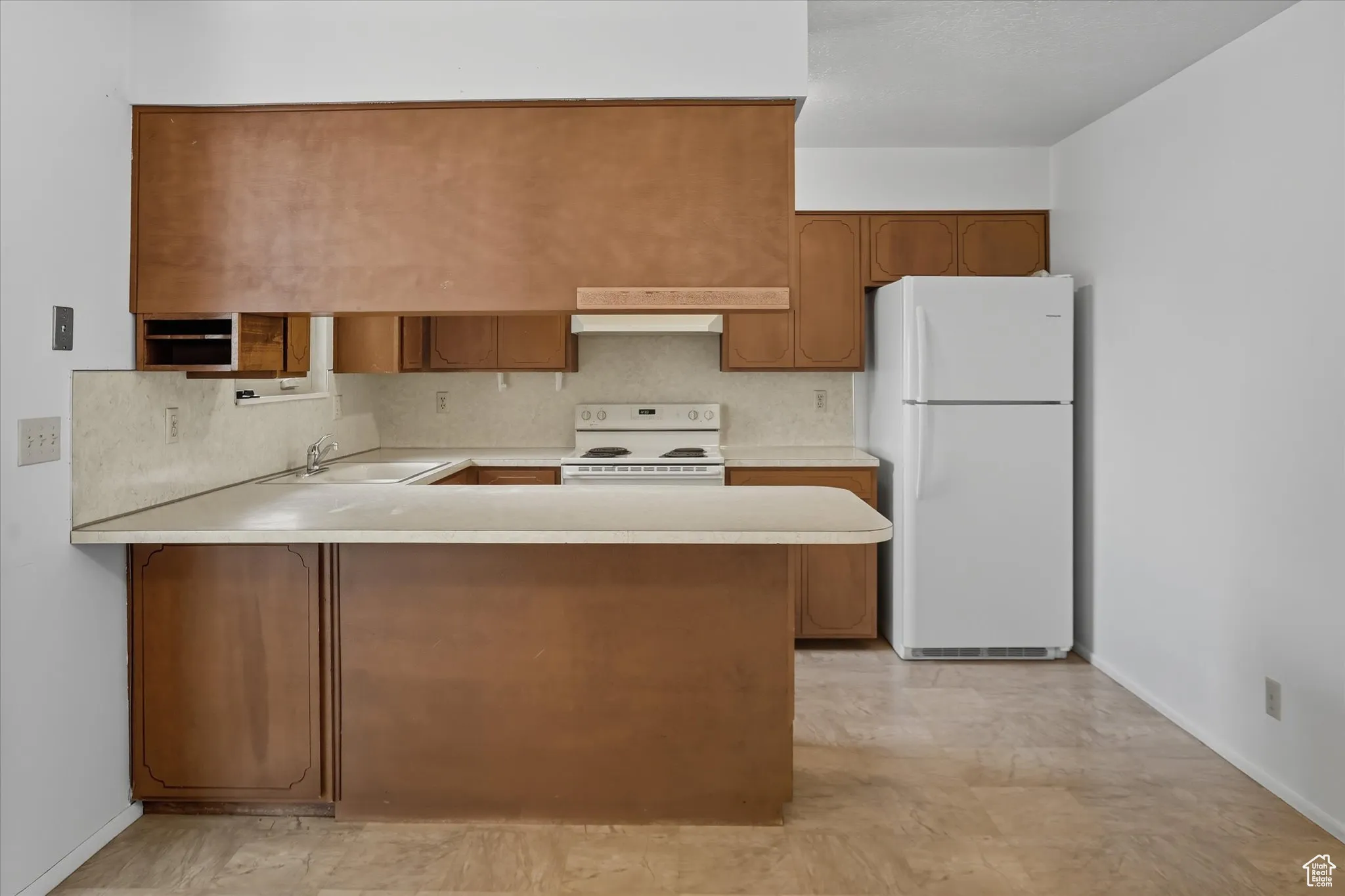 Kitchen featuring light countertops, brown cabinets, white appliances, a peninsula