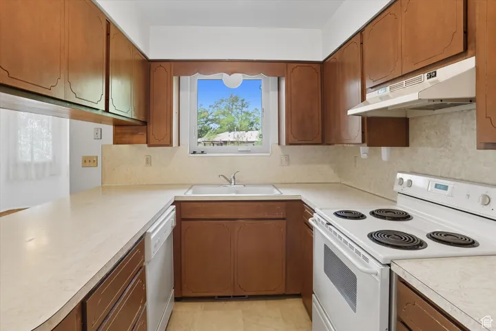 Kitchen with white range with electric stovetop, light countertops, brown cabinets, under cabinet range hood, and dishwasher