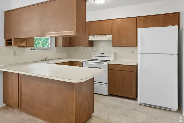 Kitchen featuring white appliances, brown cabinetry, light countertops, a peninsula