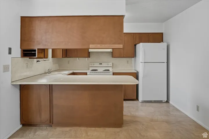 Kitchen featuring light countertops, brown cabinets, white appliances, a peninsula
