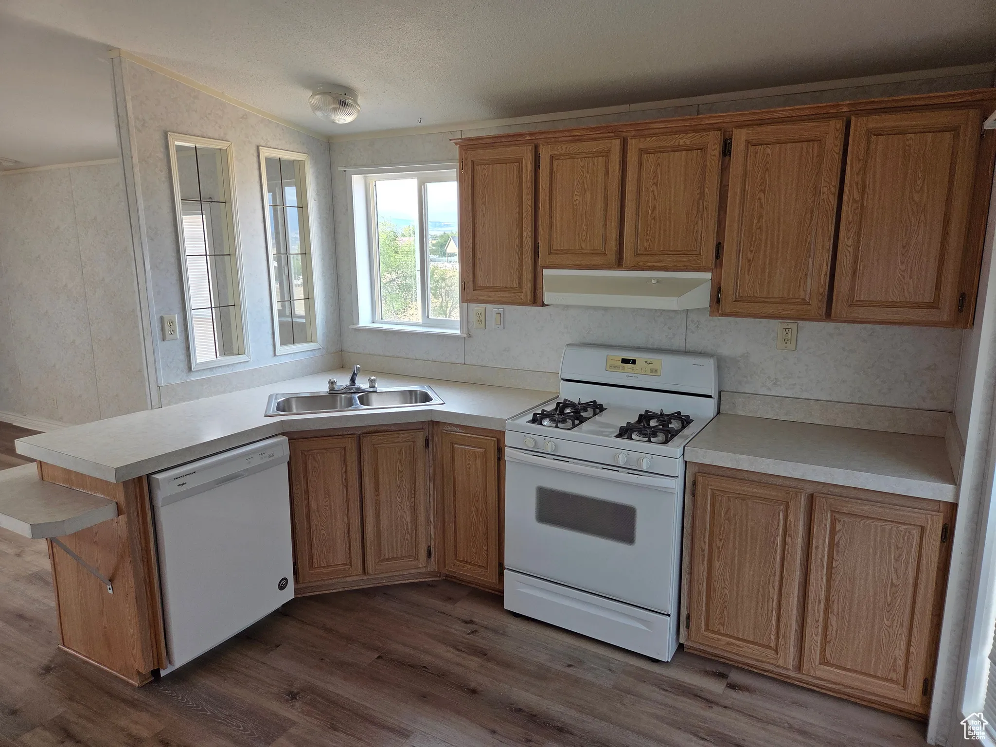 Kitchen featuring white appliances, dark wood finished floors, light countertops, under cabinet range hood, and wallpapered walls
