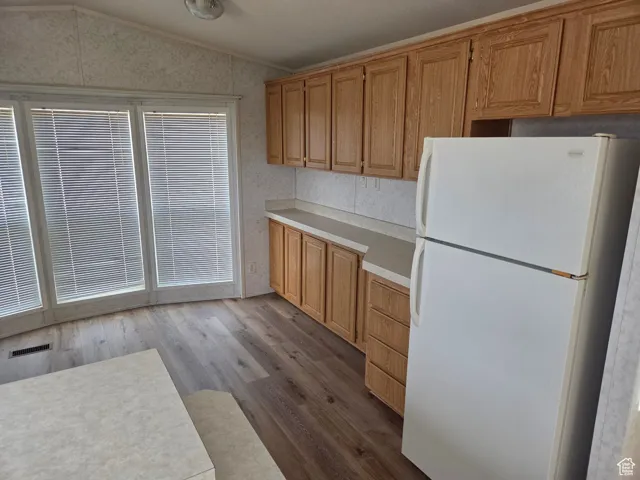 Kitchen featuring freestanding refrigerator, light countertops, dark wood-style floors, lofted ceiling, and brown cabinets