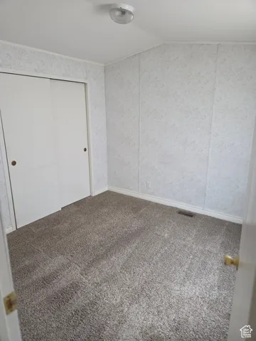 Unfurnished bedroom with carpet flooring, vaulted ceiling, and a closet