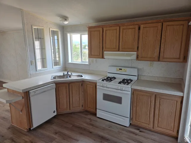 Kitchen featuring white appliances, dark wood finished floors, light countertops, under cabinet range hood, and wallpapered walls