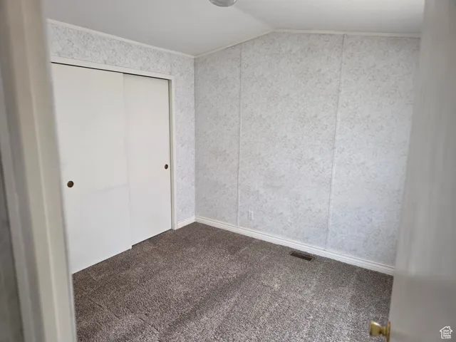 Unfurnished bedroom with carpet, vaulted ceiling, and a closet