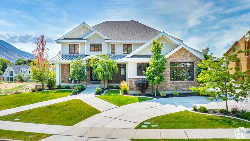 Craftsman-style home featuring a front lawn, a shingled roof, stone siding, a standing seam roof, and a metal roof