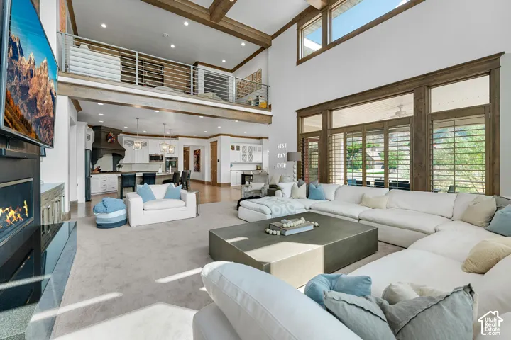 Living area featuring a glass covered fireplace, healthy amount of natural light, beam ceiling, recessed lighting, and carpet floors
