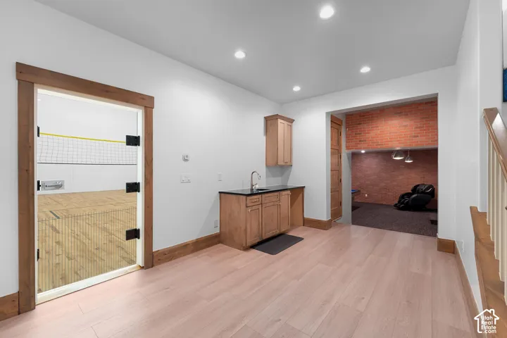 Bar featuring light wood-type flooring, brick wall, recessed lighting, and dark stone countertops