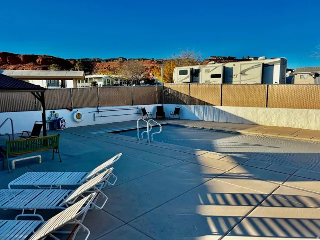 Outdoor pool area with concrete decking and metal handrails, surrounded by a privacy fence and a red rock backdrop