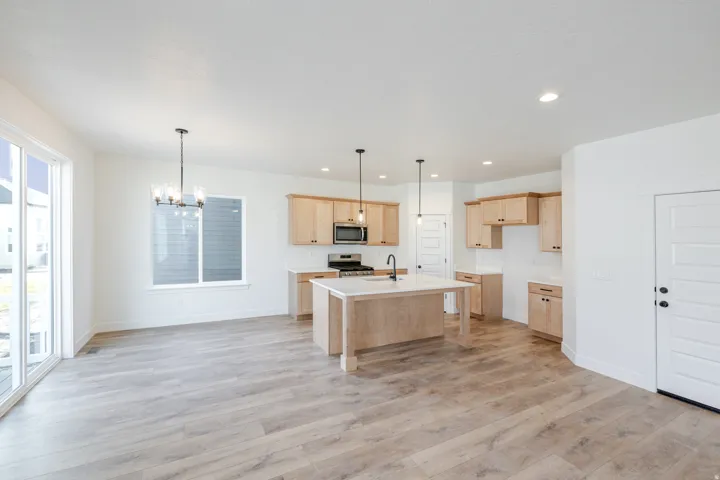 Kitchen with light wood finish cabinetry, light wood-style flooring, suspended lighting, stainless steel appliances, and a center island with sink
