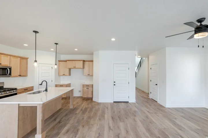 Kitchen featuring light wood-style floors, pendant lighting, a ceiling fan, a breakfast bar area, and stainless steel appliances