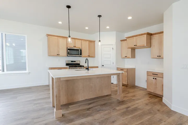 Kitchen with light wood finish cabinetry, hanging light fixtures, stainless steel appliances, and light wood finished floors