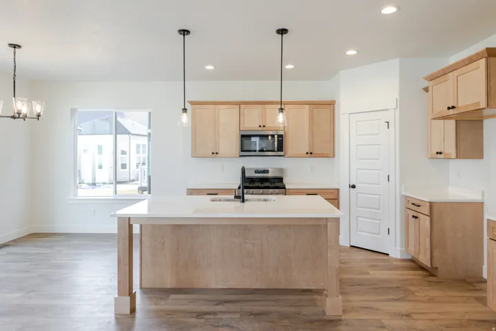 Kitchen with light wood finish cabinetry, a chandelier, stainless steel appliances, and light wood-type flooring