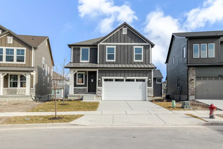 View of front of home with board and batten siding, an attached garage, driveway, and stone siding