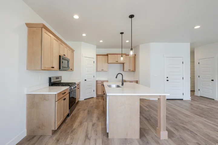 Kitchen featuring stainless steel appliances, light wood finish cabinetry, hanging light fixtures, a center island with sink, and light wood finished floors