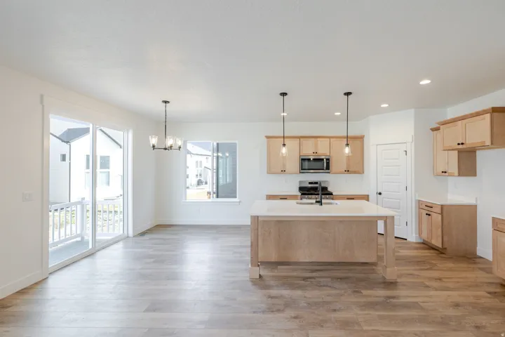 Kitchen featuring stainless steel appliances, suspended lighting, light wood-style floors, and light wood finish cabinets