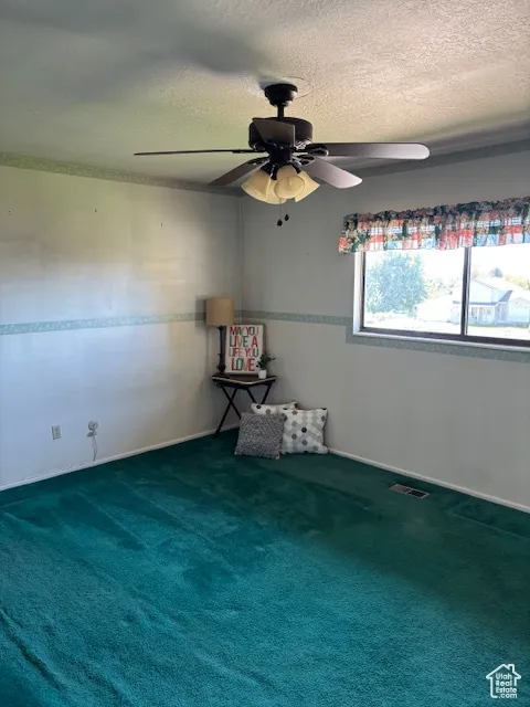 Spare room with a textured ceiling, dark colored carpet, and a ceiling fan