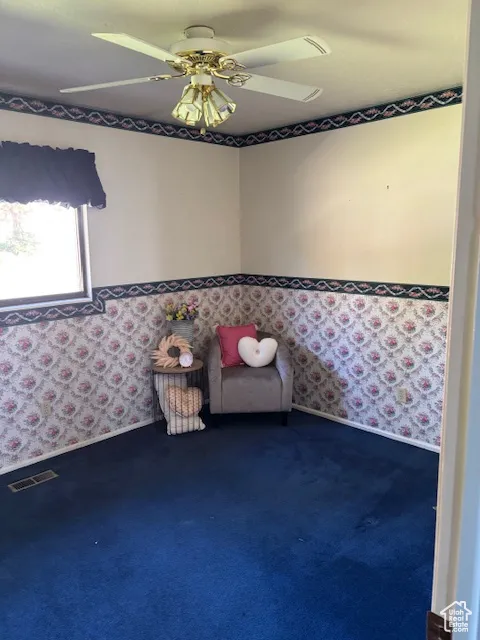 Sitting room featuring wallpapered walls, a ceiling fan, and dark colored carpet