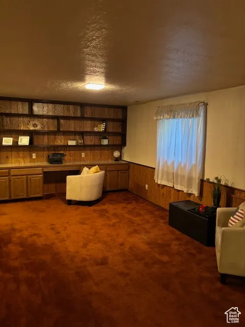 Sitting room featuring wood walls, a wainscoted wall, dark carpet, and a textured ceiling