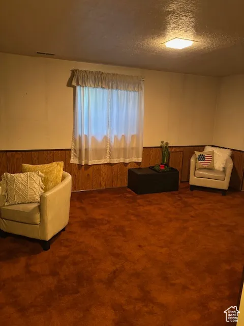 Carpeted living room with wooden walls, a wainscoted wall, and a textured ceiling