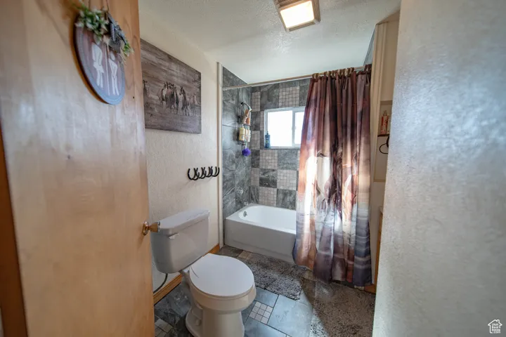Bathroom with a textured wall, shower / bath combo with shower curtain, and a textured ceiling