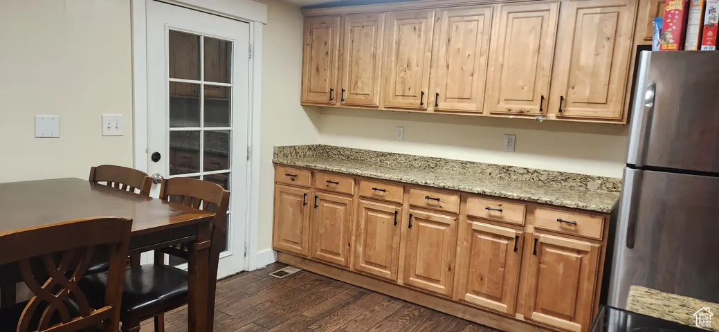 Kitchen featuring freestanding refrigerator, light stone counters, and dark wood-type flooring