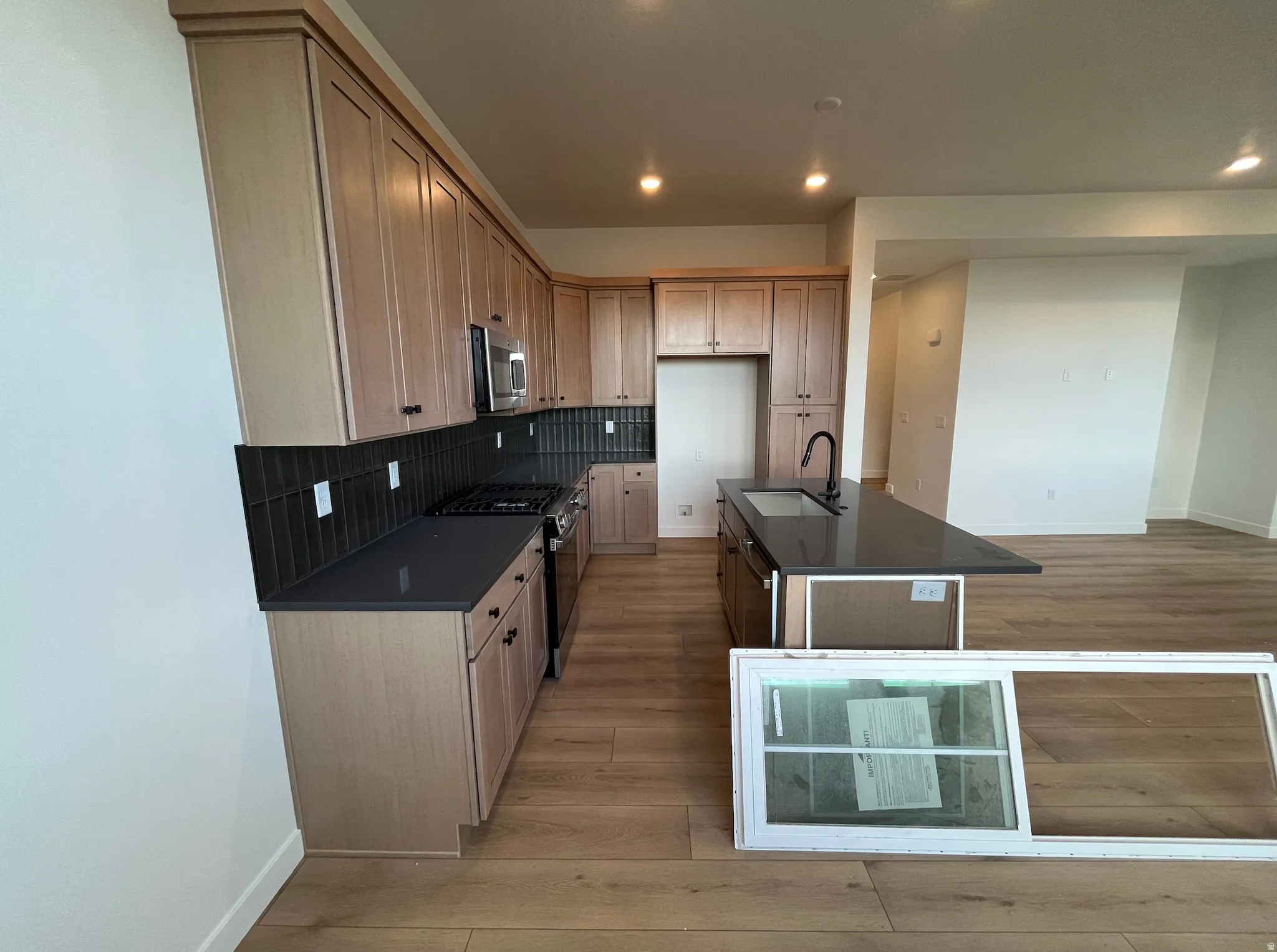 Kitchen featuring decorative backsplash, stainless steel appliances, a center island with sink, light wood finished floors, and recessed lighting