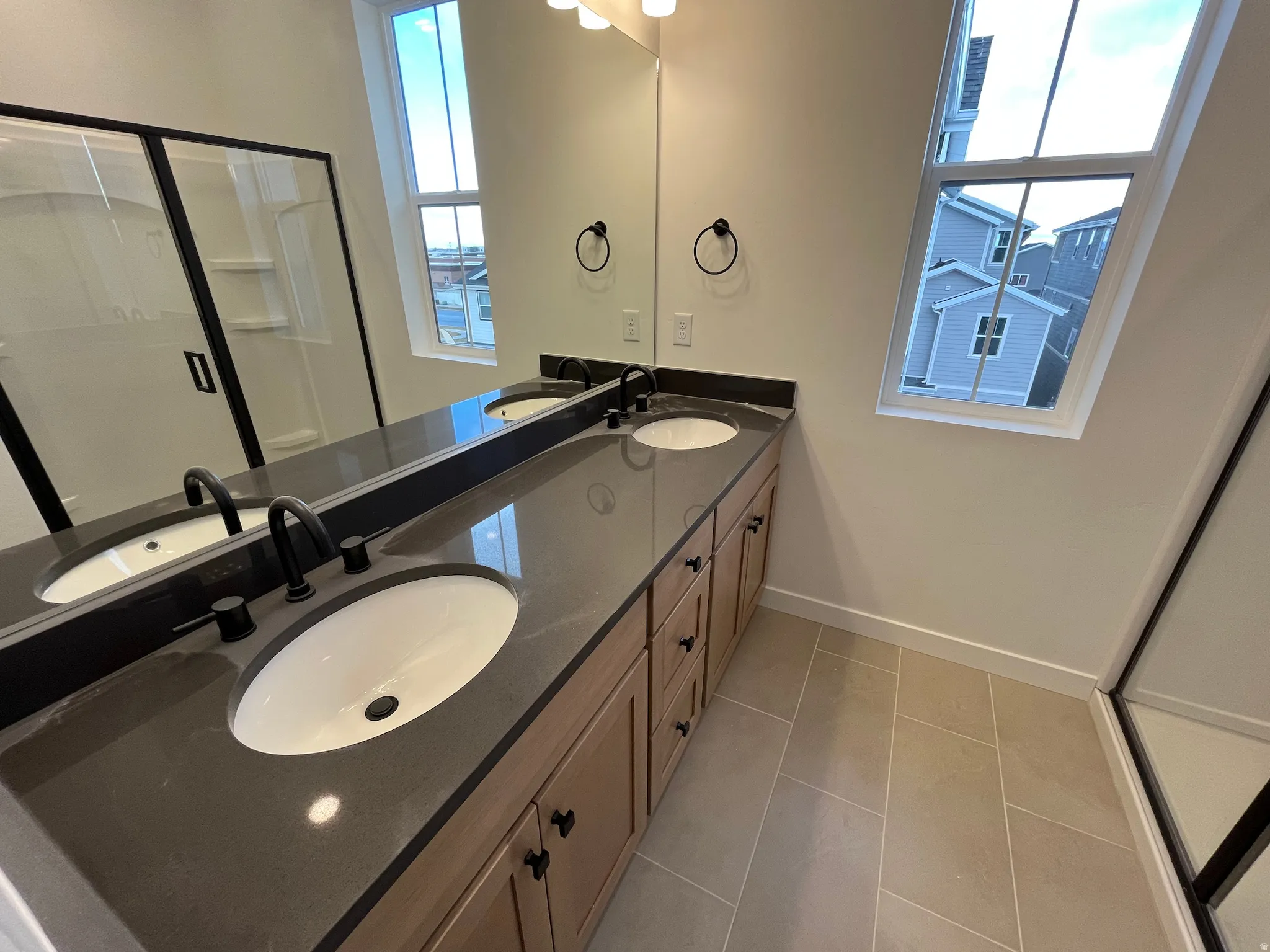 Bathroom featuring a shower stall, double vanity, and light tile patterned flooring