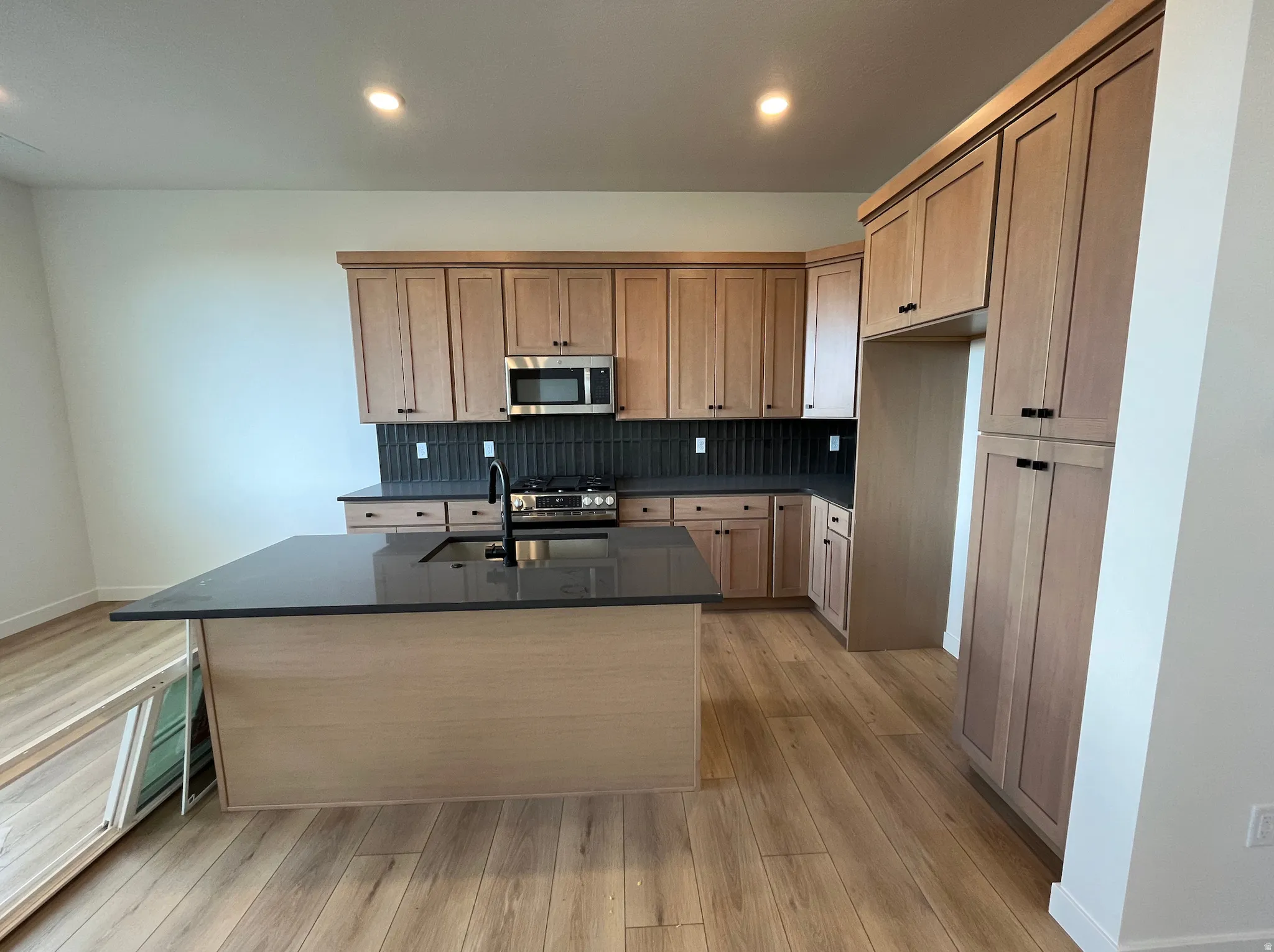 Kitchen featuring stainless steel appliances, tasteful backsplash, dark stone counters, an island with sink, and light wood-style floors