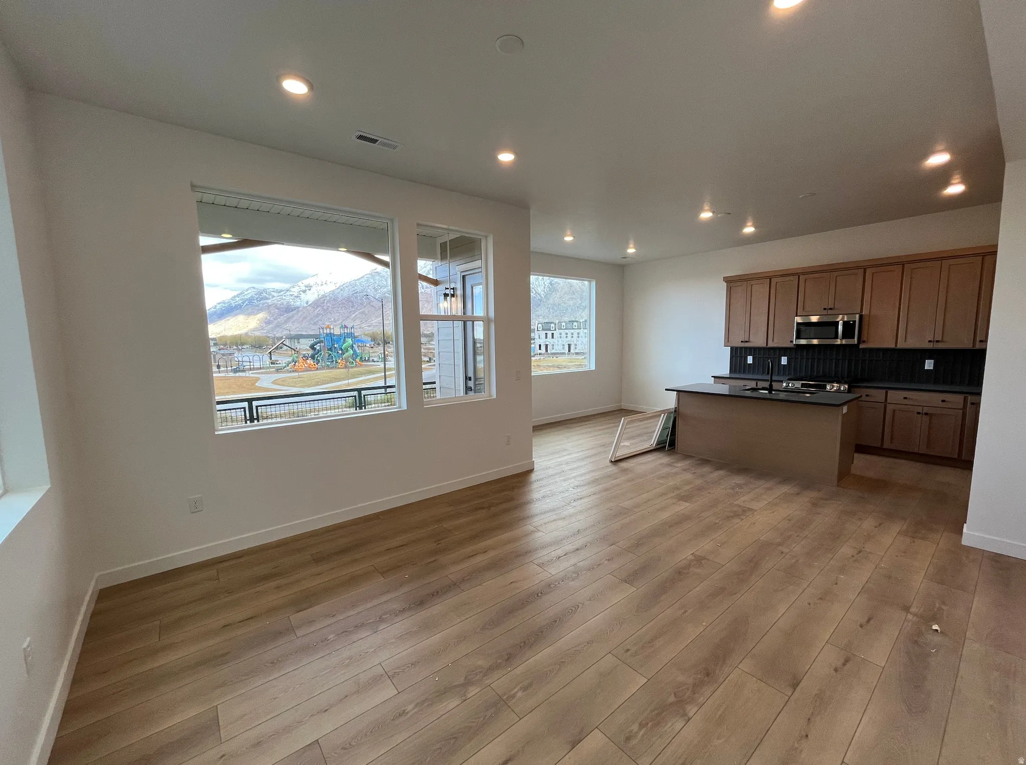 Kitchen with dark countertops, a center island with sink, open floor plan, decorative backsplash, and stainless steel microwave