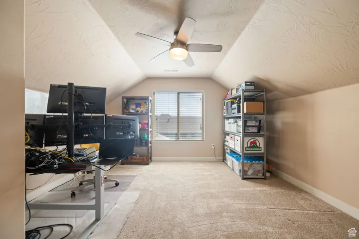 Carpeted office featuring a textured ceiling, lofted ceiling, and ceiling fan