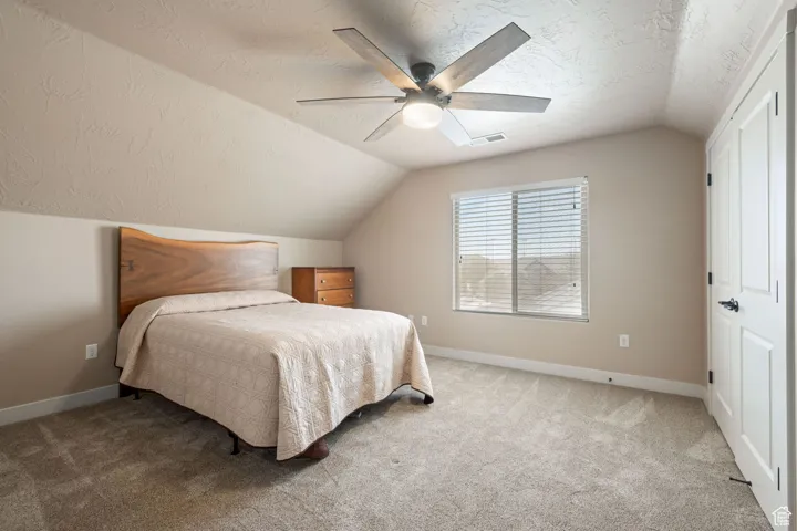 Bedroom with vaulted ceiling, a textured ceiling, carpet flooring, and ceiling fan