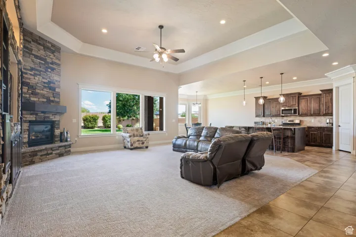 Living room with a raised ceiling, recessed lighting, a fireplace, a ceiling fan, and crown molding