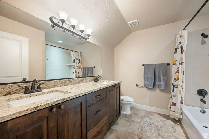 Bathroom featuring shower / tub combo, double vanity, vaulted ceiling, and a textured ceiling