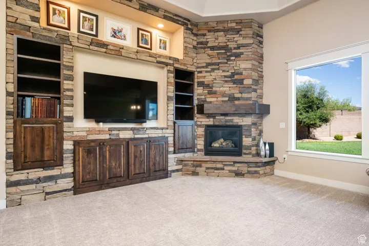 Living room featuring an outdoor stone fireplace, carpet floors, and built in features