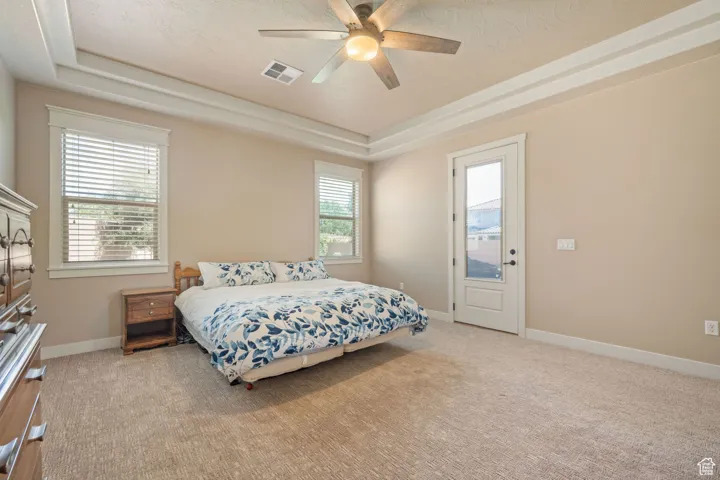 Bedroom featuring a raised ceiling, light carpet, a ceiling fan, and access to exterior