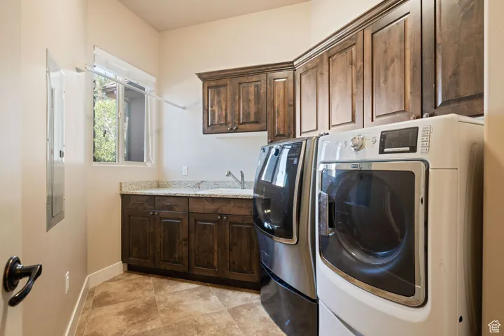 Washroom with cabinet space, washer and dryer, light tile patterned floors, and electric panel