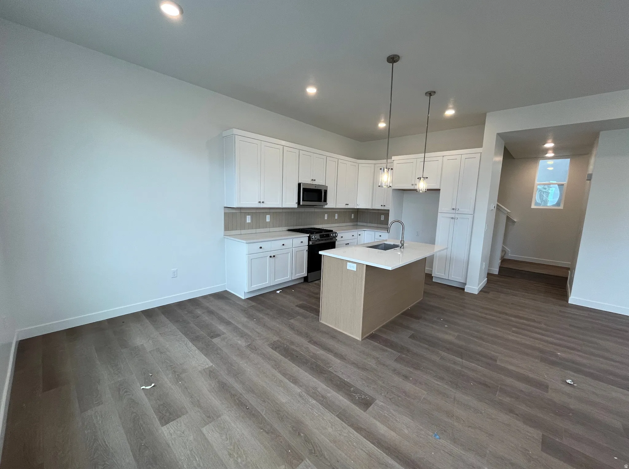 Kitchen featuring white cabinetry, black gas range, hanging light fixtures, an island with sink, and recessed lighting