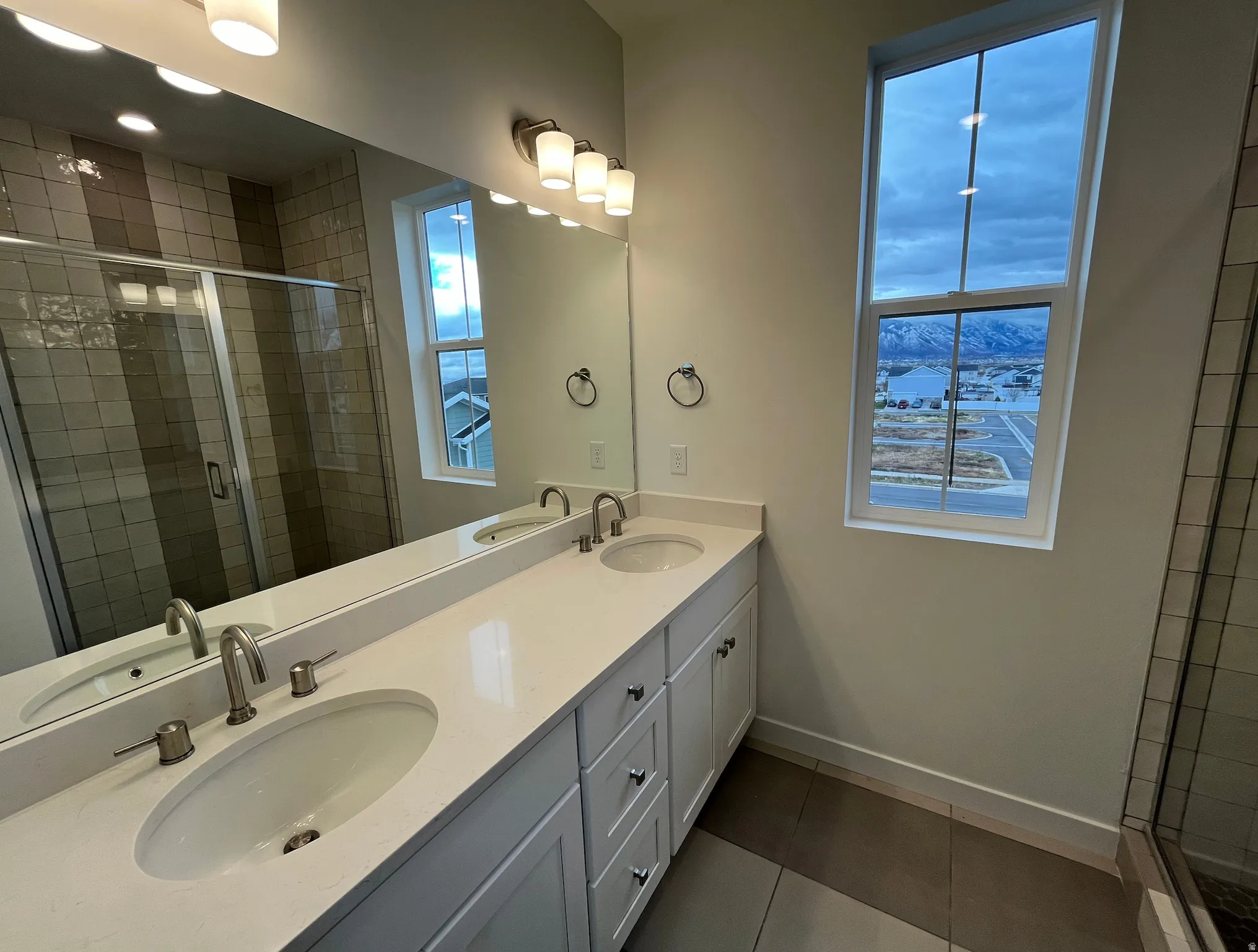 Full bathroom featuring a stall shower, double vanity, and dark tile patterned flooring