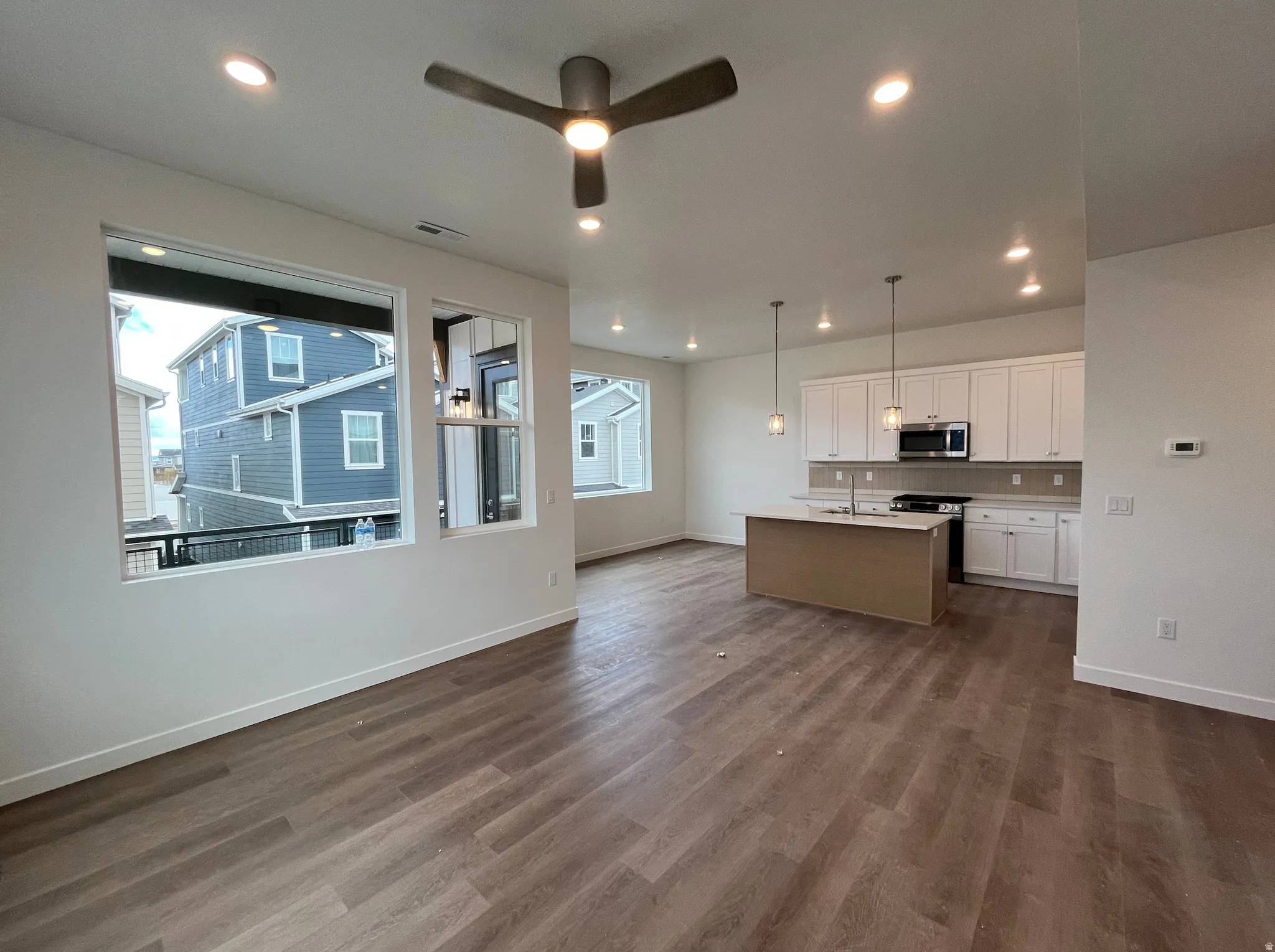 Kitchen featuring white cabinetry, open floor plan, ceiling fan, a center island with sink, and decorative light fixtures