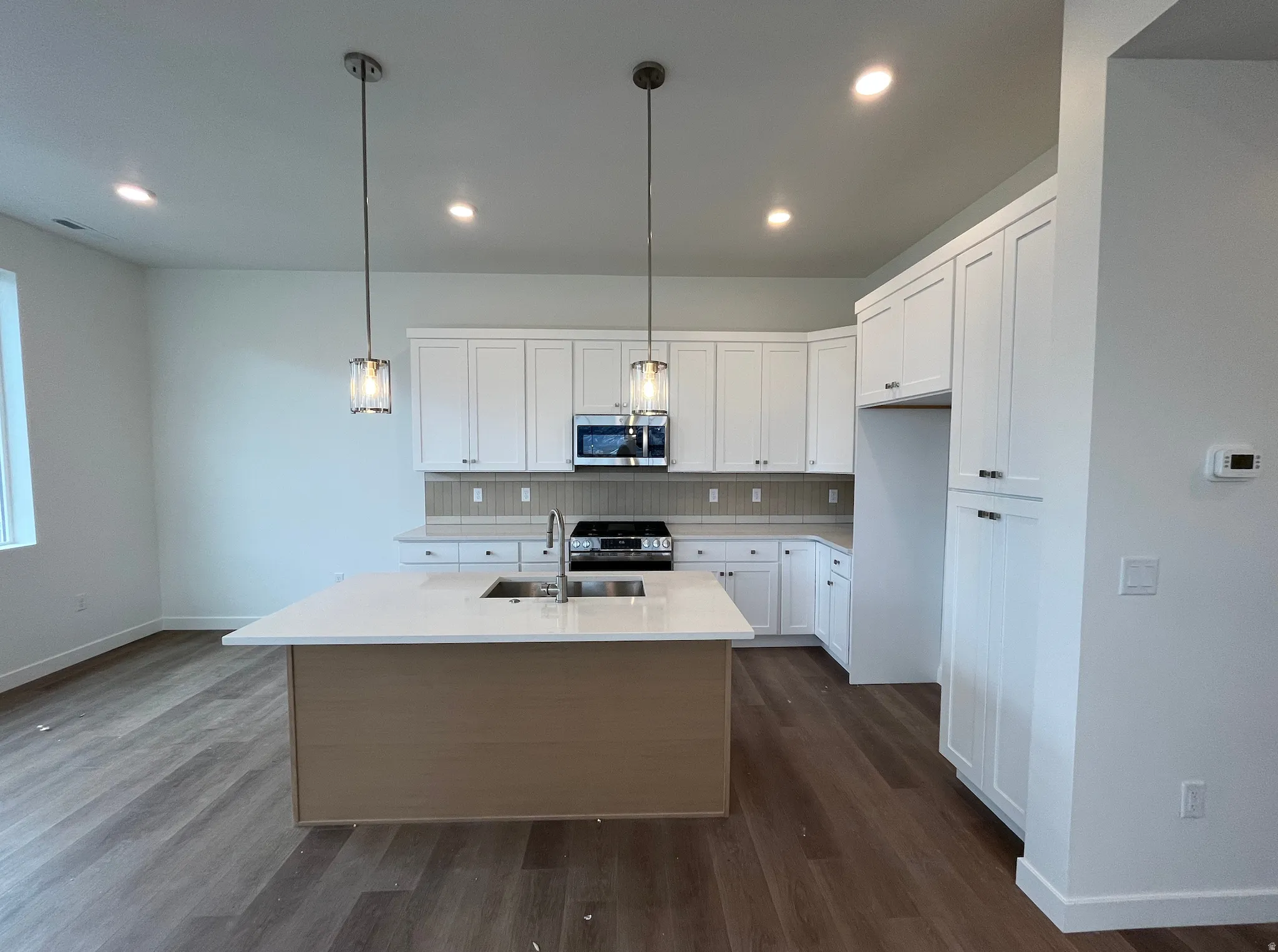 Kitchen featuring a center island with sink, white cabinets, decorative backsplash, appliances with stainless steel finishes, and decorative light fixtures