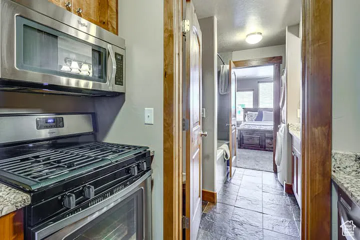 2nd Kitchen with stainless steel appliances, brown cabinetry, stone tile floors, and light stone countertops
