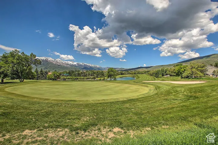 View of community with view of golf course, a water and mountain view, and a lawn